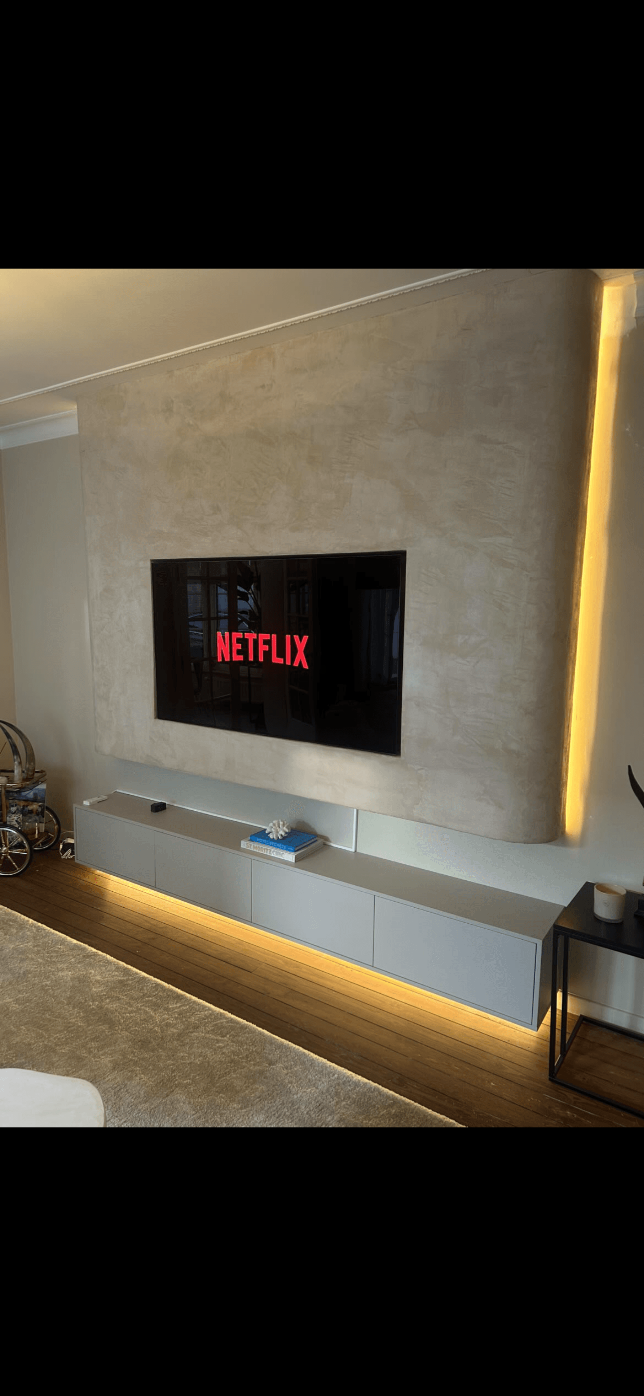 Accentwand in Mortex met zachte wolktekening en indirecte verlichting langs de randen, met een ingebouwde televisie boven een zwevend tv-meubel.