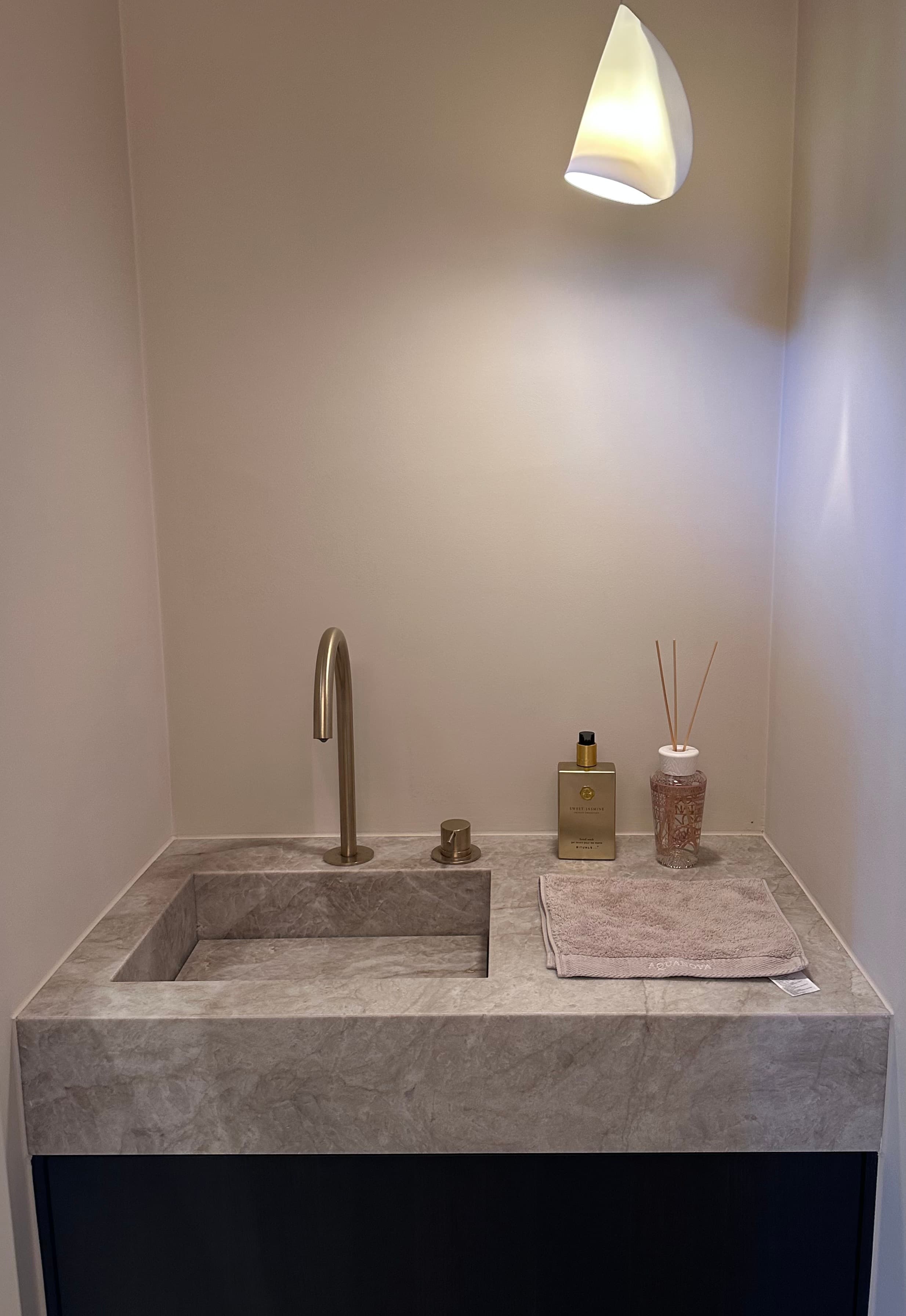 Gastentoilet met een massief natuurstenen wastafelblok, geborsteld messing kraanwerk en een warme, naadloze wandafwerking.