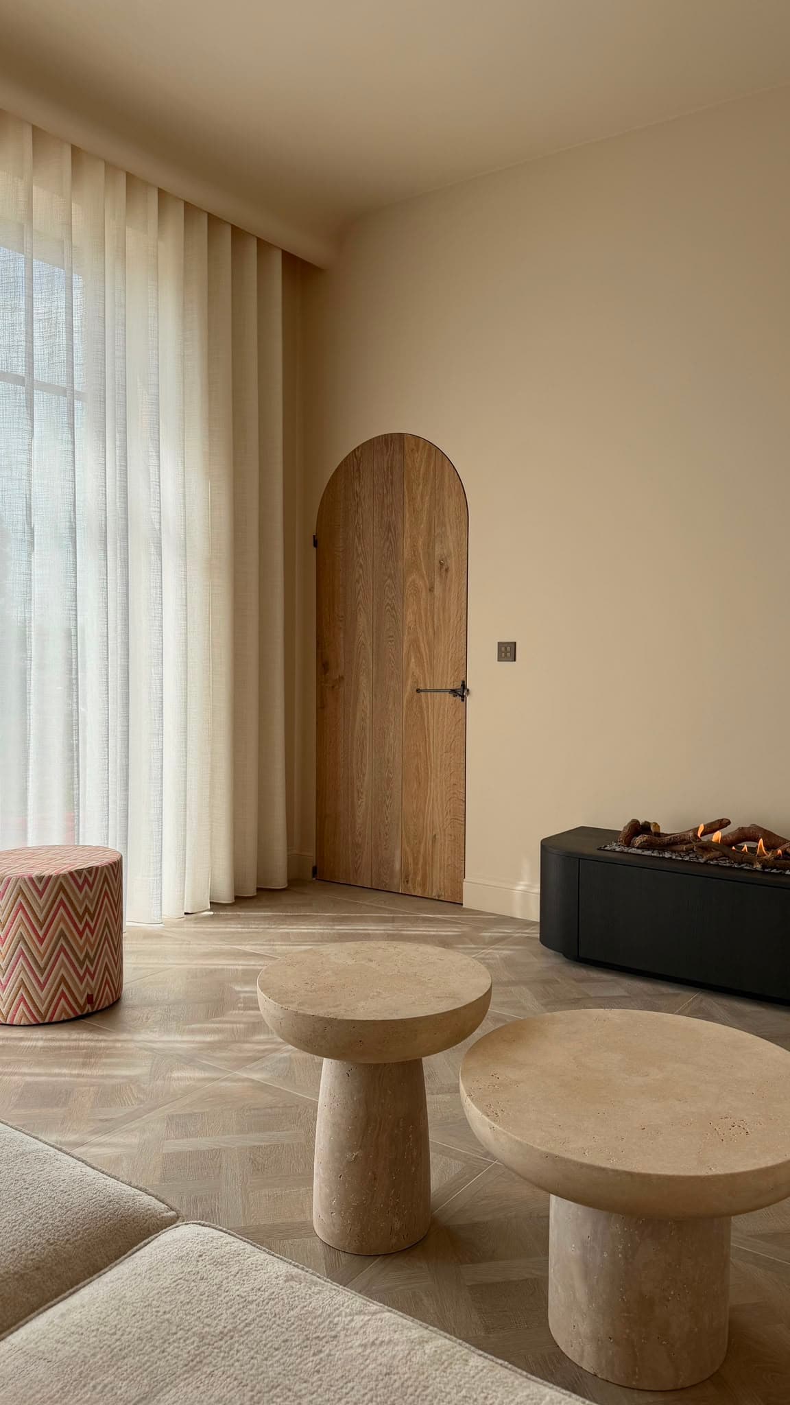 Zithoek in warme microcement met eiken boogdeur en travertin bijzettafels. Realisatie van VanDeco