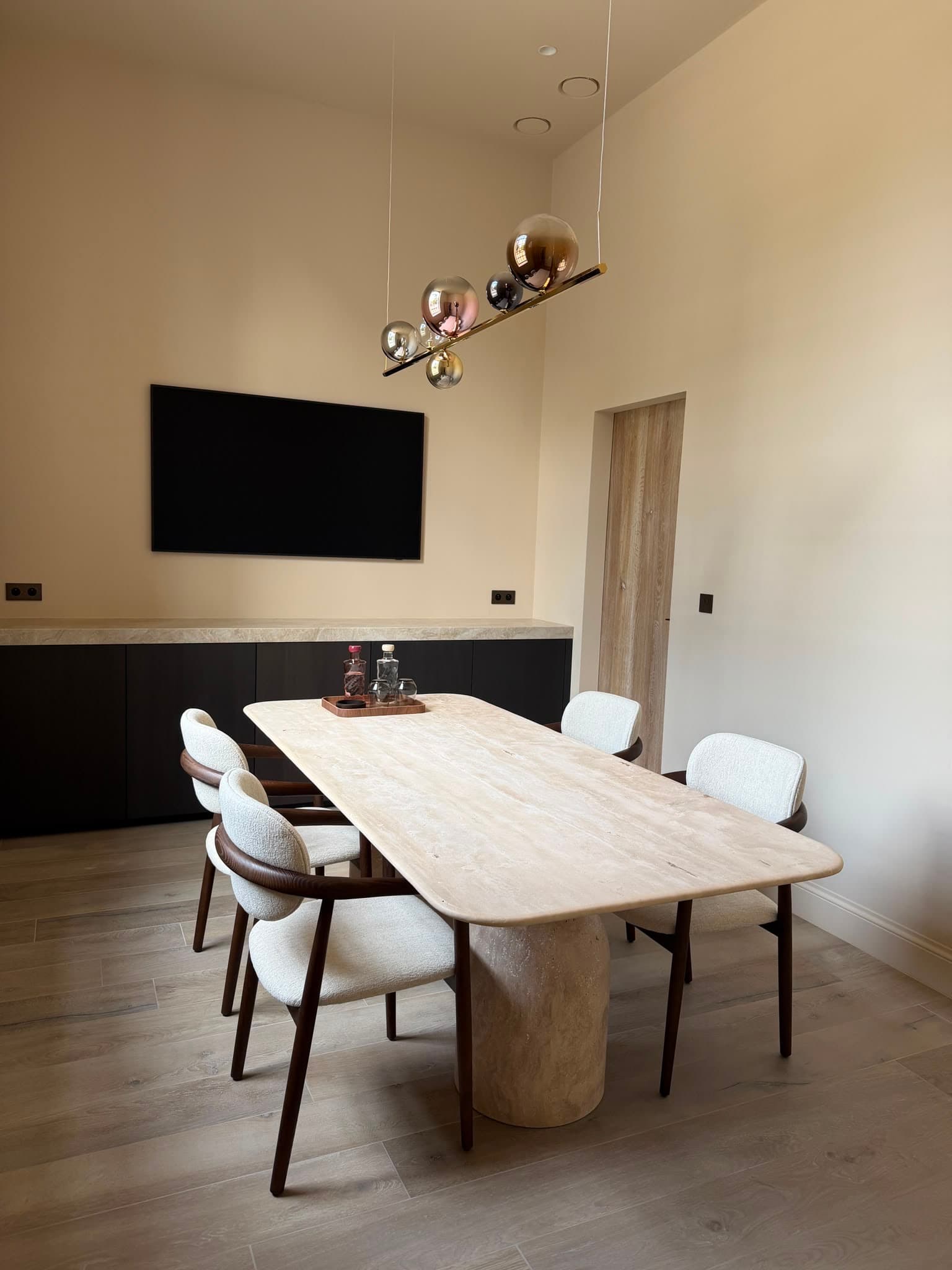 Bureauruimte met tafel, een donkere dressoirwand met stenen blad en een sculpturale hanglamp.